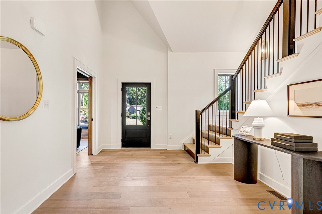 Foyer featuring vaulted ceilings, wood-finish flooring, a black paneled front door, and a staircase with stained wood treads and a black metal balustrade