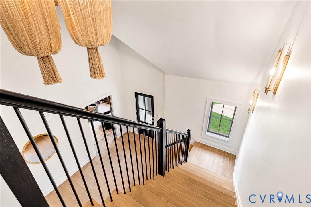 Staircase featuring wood-finish treads, matte black metal balusters, and a vaulted ceiling