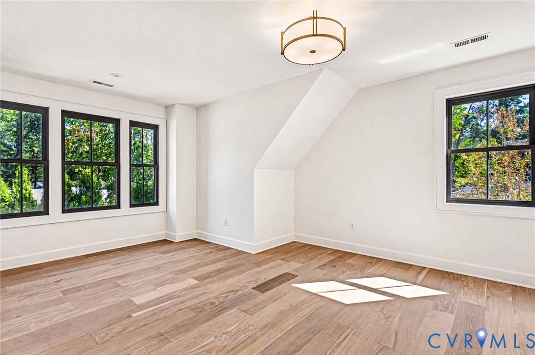 Neutral-toned room featuring wide-plank wood-finish flooring, multi-pane windows with black frames, and a modern drum-style light fixture with gold-tone metal accents