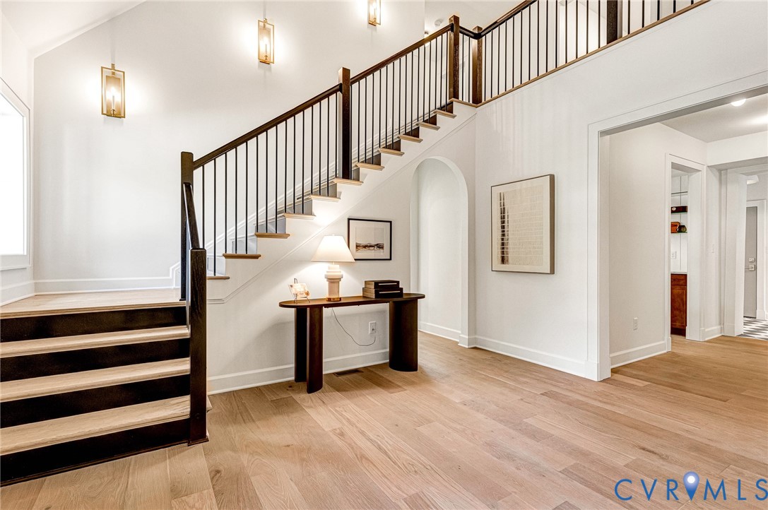 Entryway featuring wood-finish flooring, a staircase with custom dark wood railings and balusters, vaulted ceilings, and wall-mounted geometric lantern lighting Entryway featuring wood-finish flooring, a staircase with custom dark wood railings and balusters, vaulted ceilings, and wall-mounted geometric lantern lighting