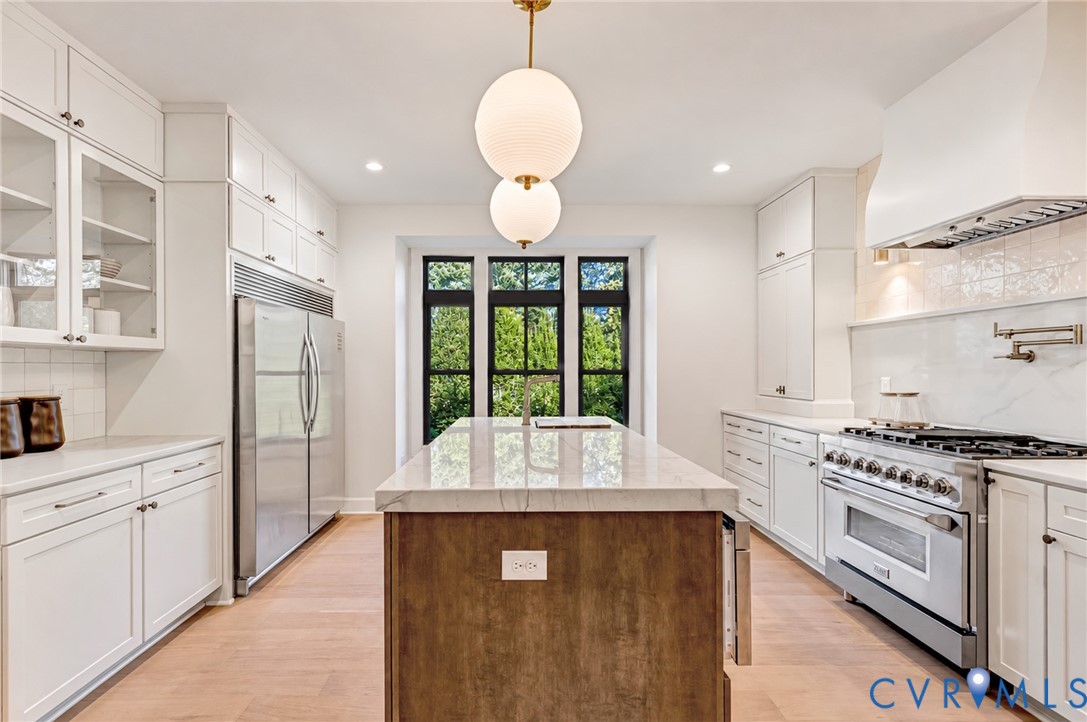 Kitchen featuring a central island with a stone-finish countertop, custom cabinetry, stainless steel professional-grade range, wood-finish flooring, and globe-style pendant lighting