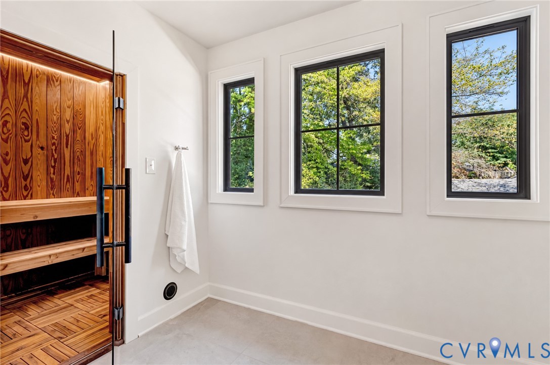 Custom built-in sauna with wood-panel detailing, glass door entry, and integrated lighting, complemented by large-format tile flooring and mullioned windows with black frames