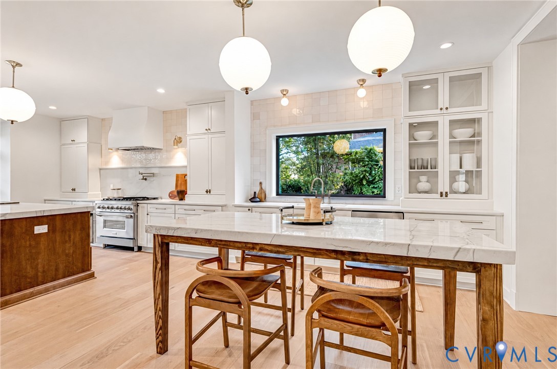 Kitchen featuring stone countertops, integrated wood-finish cabinetry, a professional-grade gas range with a custom hood, and globe pendant lighting Kitchen featuring stone countertops, integrated wood-finish cabinetry, a professional-grade gas range with a custom hood, and globe pendant lighting