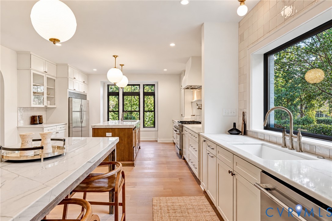 Kitchen featuring custom white cabinetry, stone countertops, wood-finish flooring, a central island with wood base, and globe pendant lighting