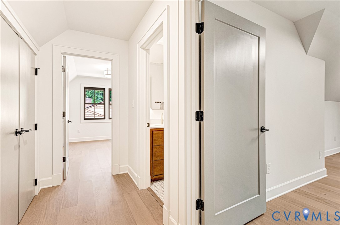 Interior hall featuring light-tone wood-finish flooring, shaker-style interior doors, matte black hardware, and crisp white trim