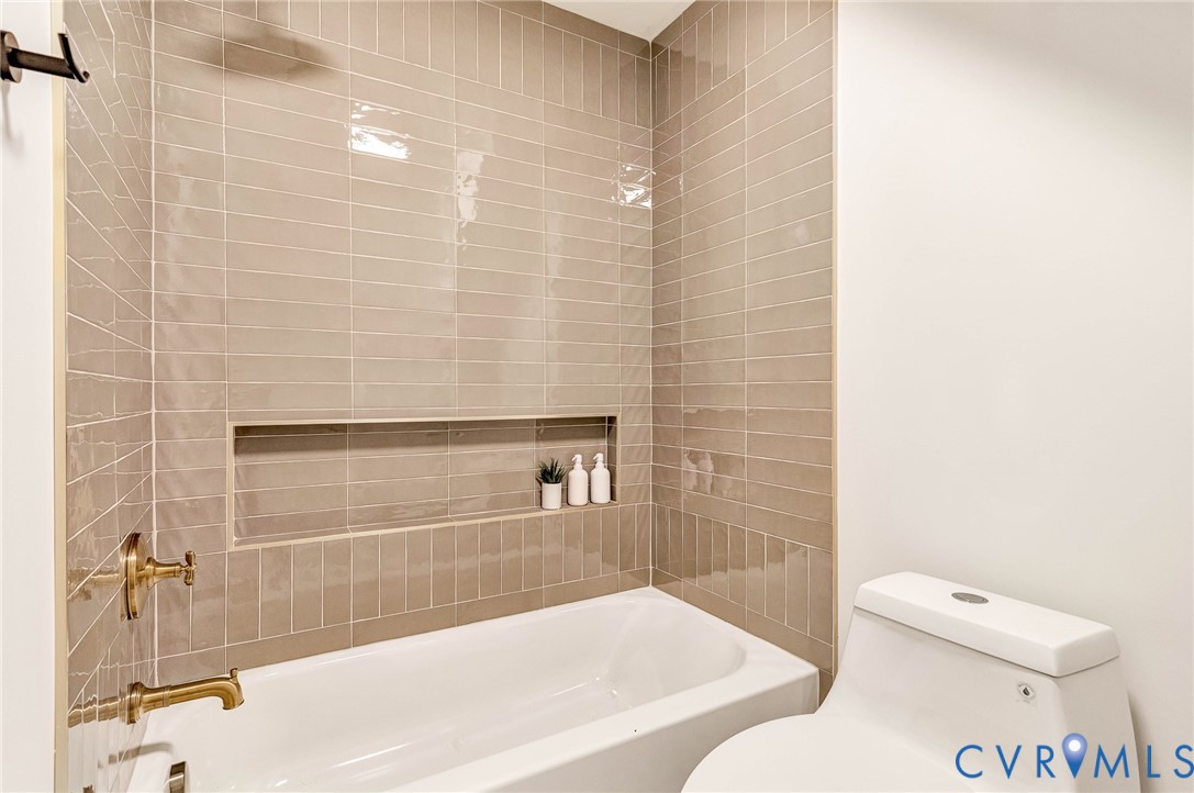 Bathtub surround featuring vertically stacked, glossy taupe subway tiles, a recessed wall niche, and brass-finish plumbing fixtures