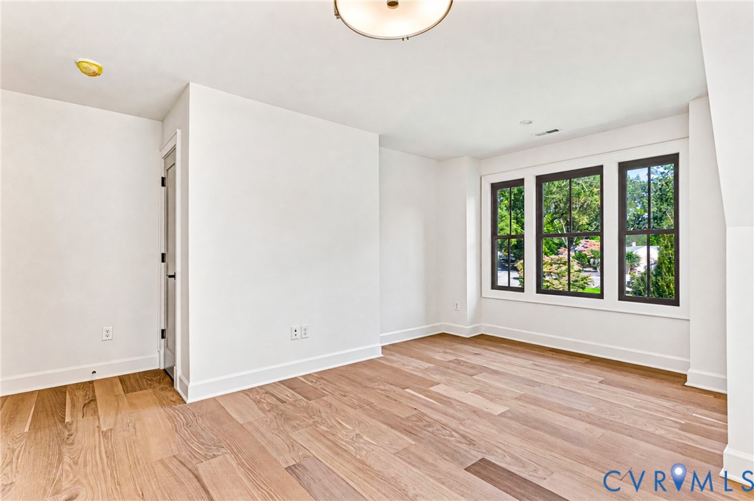 Interior room featuring wood-finish flooring, a triple-pane window configuration with dark frames, and a central ceiling-mounted flush light fixture