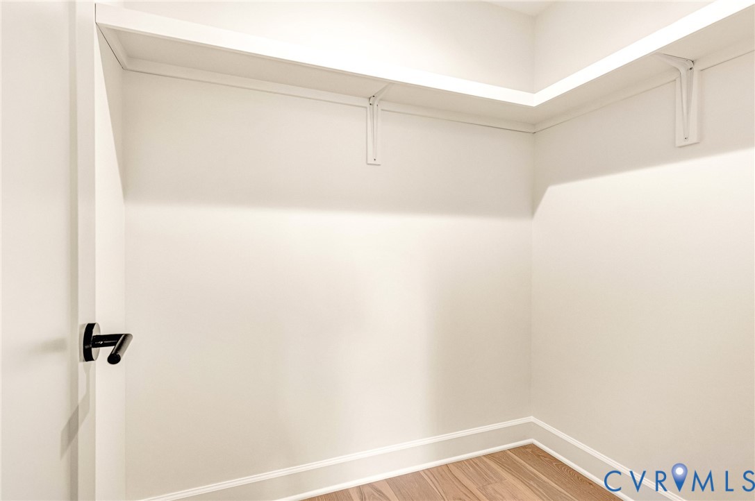 Walk-in closet featuring white wall-mounted shelving with bracket supports, wood-finish flooring, and a matte black lever door handle