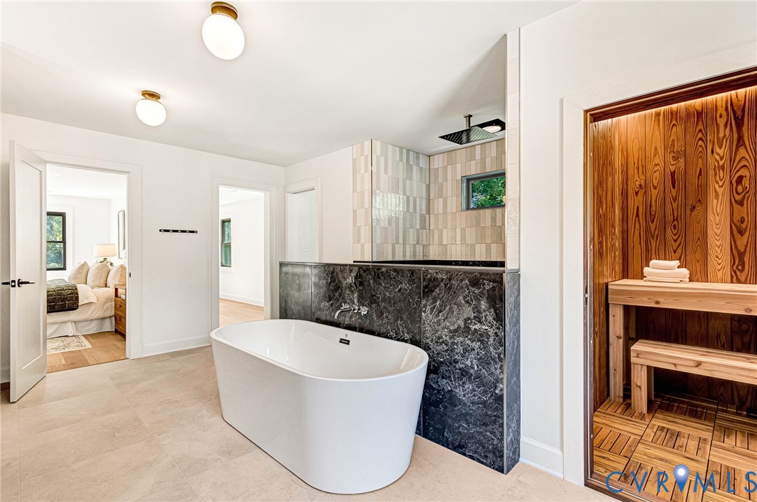 Freestanding white soaking tub with wall-mounted faucet, stone-surround shower area, and built-in sauna featuring wood paneling and bench seating