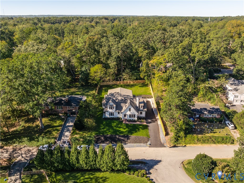 Aerial perspective of a detached residence featuring a multi-gabled roofline, light-colored siding, an asphalt driveway, and a fenced-in rear lawn surrounded by mature trees