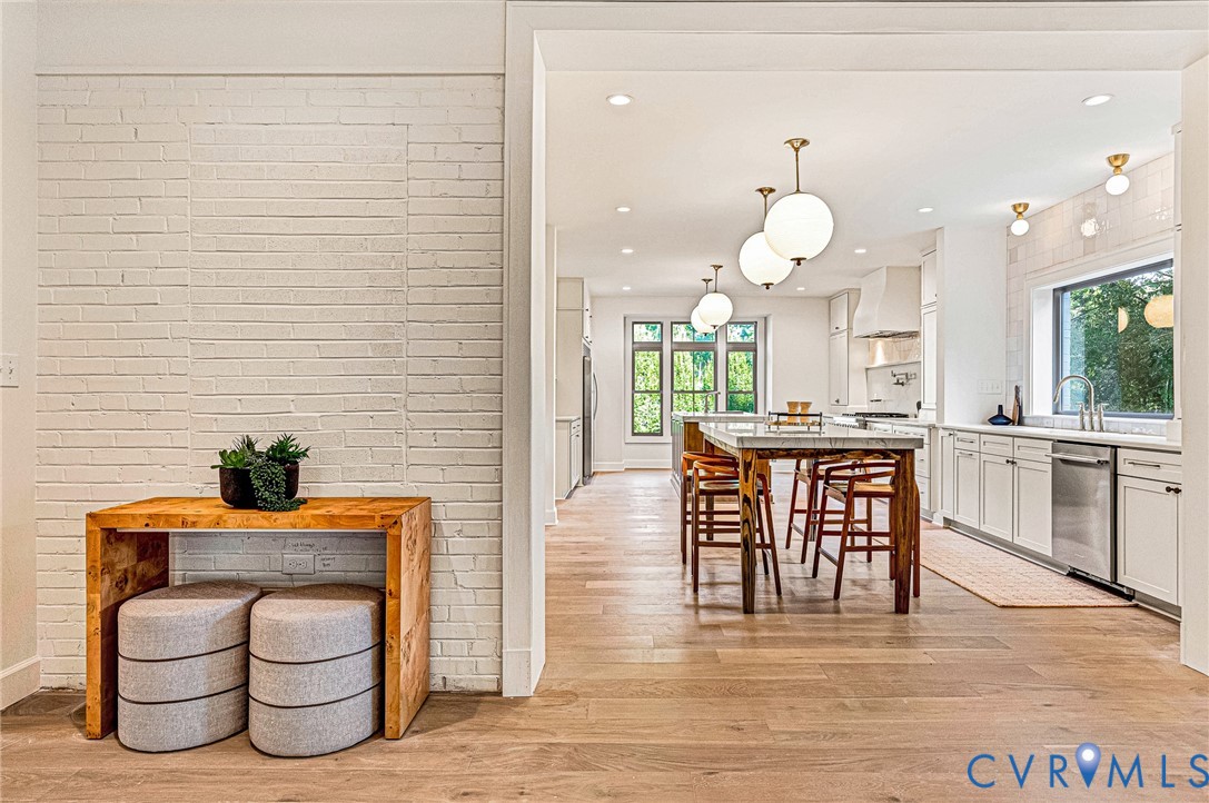 Painted white brick wall, wood-finish flooring, white cabinetry, integrated stainless steel appliances, and spherical pendant lighting