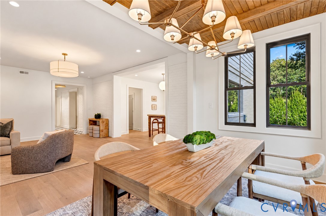 Wood-plank ceiling with exposed beams, custom multi-light chandelier, wood-finish flooring, and crisp white-painted brick accent walls
