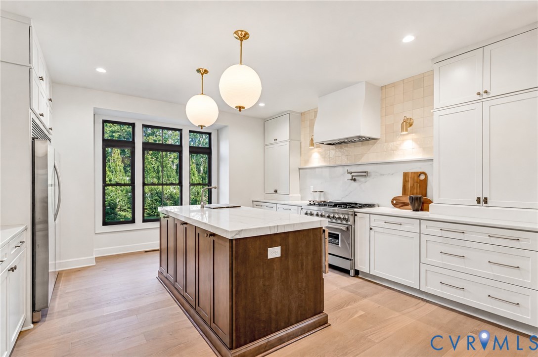 Gourmet kitchen featuring custom cabinetry, a contrasting center island with stone-surface countertop, high-end stainless steel range, textured tile backsplash, and wood-finish flooring