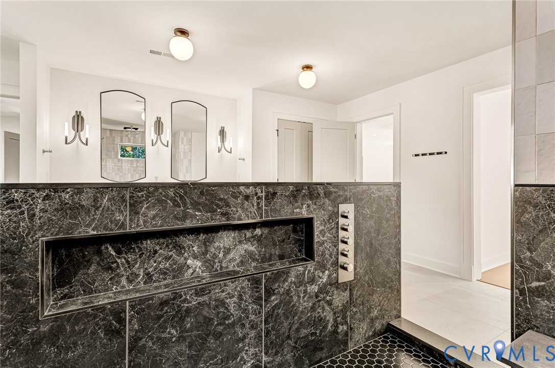 Dark stone shower partition with integrated recessed shelving, multi-head shower control panel, arched wall mirrors, dual globe ceiling fixtures, and matte metallic wall sconces
