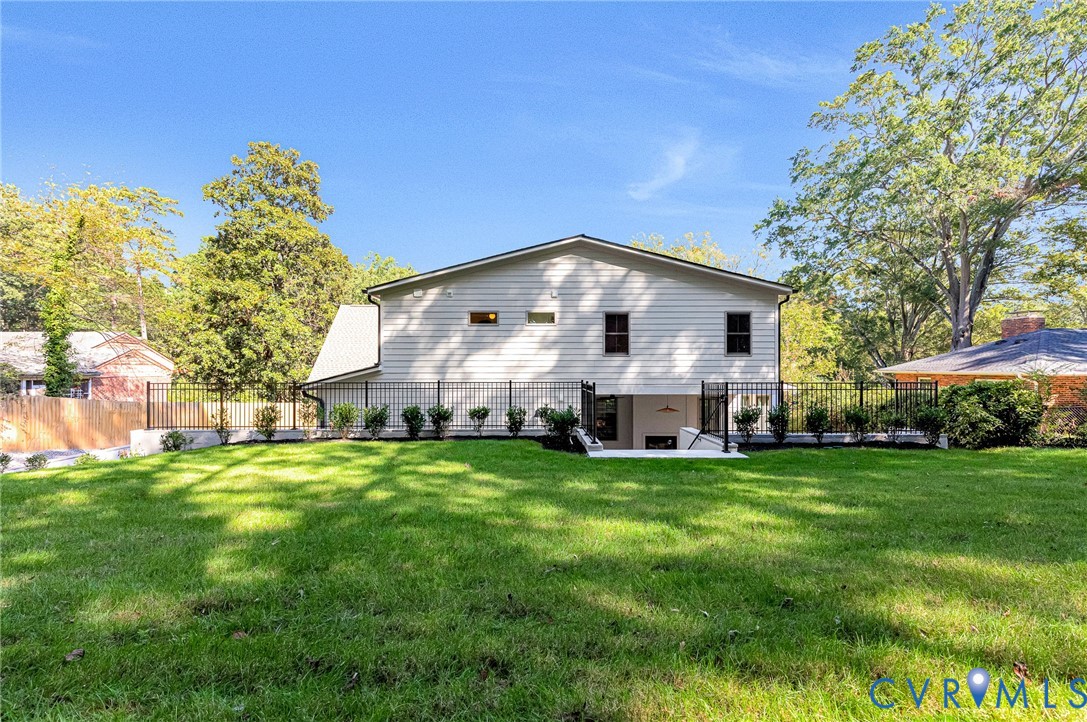 Expansive backyard featuring a manicured lawn, perimeter metal fencing, and established perimeter shrubbery