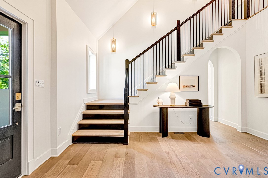 Foyer featuring wood-finish flooring, a vaulted ceiling, a staircase with custom metal railing, and arched architectural details Foyer featuring wood-finish flooring, a vaulted ceiling, a staircase with custom metal railing, and arched architectural details