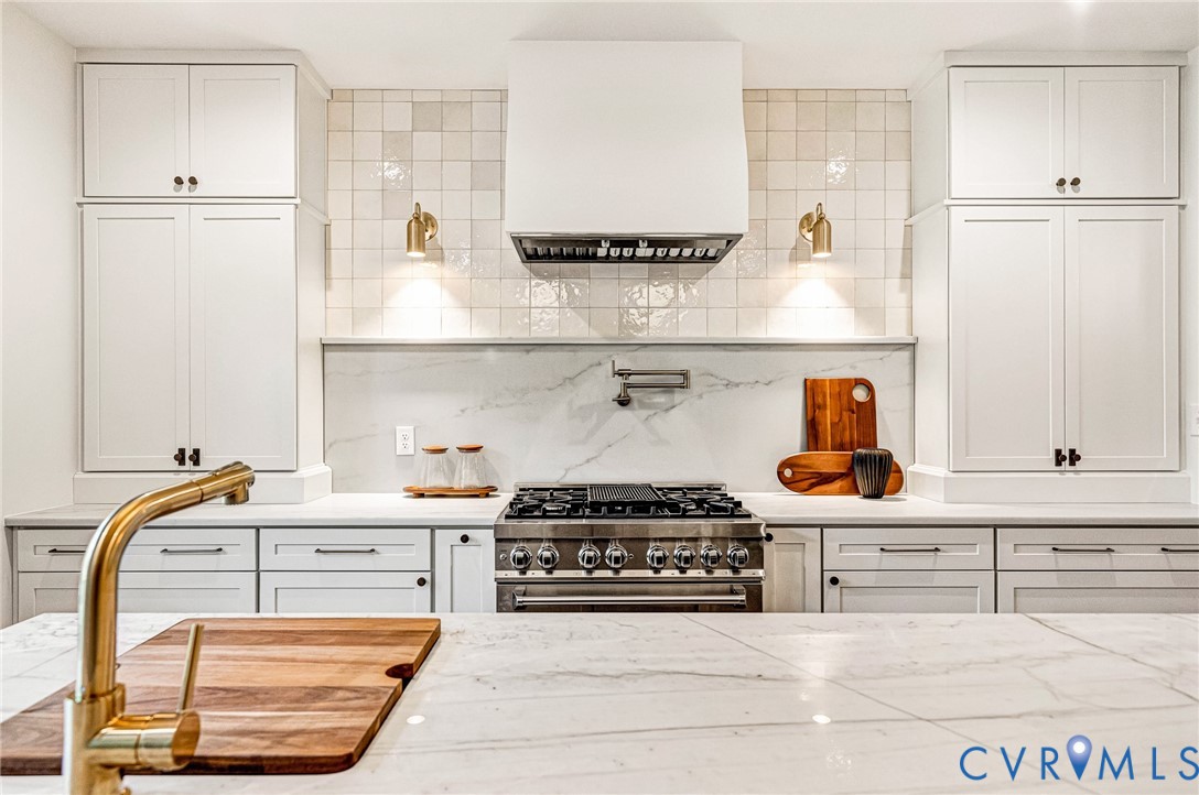 Kitchen featuring floor-to-ceiling Shaker-style cabinetry, a custom range hood, square-tiled backsplash, stone-look countertops, and a professional-grade gas range with a wall-mounted pot filler