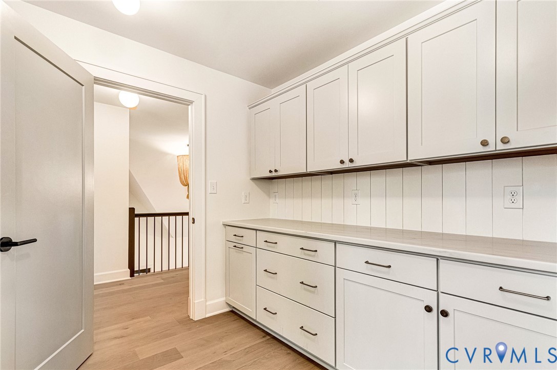 Custom cabinetry with Shaker-style doors, stone-finish countertops, vertical shiplap backsplash, and wood-finish flooring