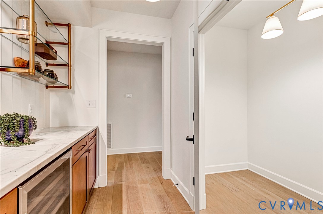 Custom cabinetry with stone-surface countertop, built-in under-counter beverage refrigerator, tiered metal wall shelving, and light-tone wood-finish flooring