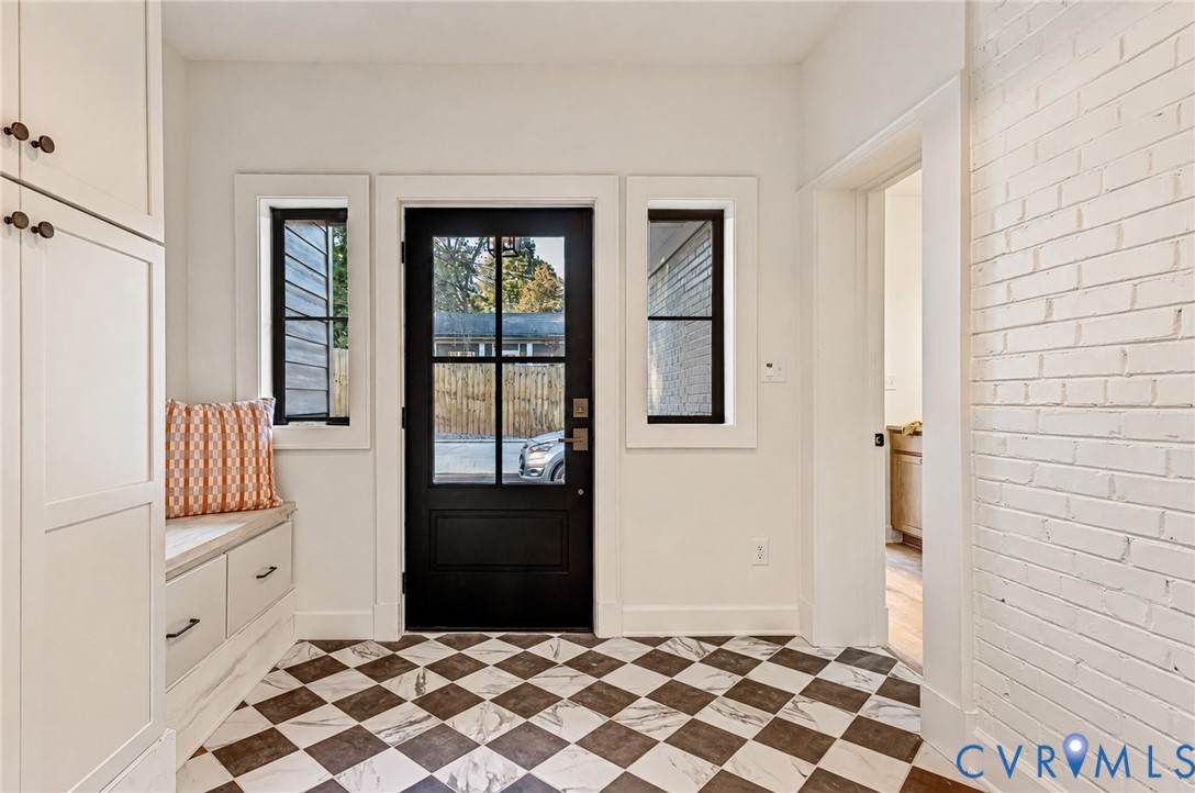 Entryway featuring a black-paned glass door, checkerboard tile flooring, built-in cabinetry with bench seating, and a painted white brick accent wall
