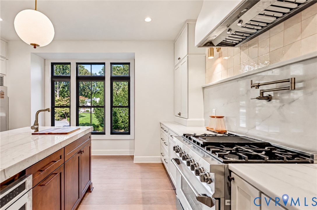 Kitchen featuring a professional-grade stainless steel range, white stone countertops, custom cabinetry with a wood-finish island, a wall-mounted pot filler, and oversized windows with black frames