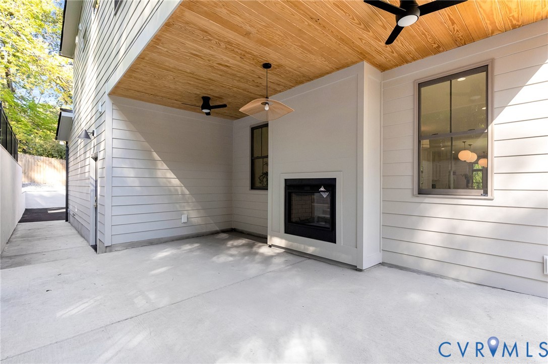 Covered patio featuring a concrete floor, wood-plank ceiling, built-in outdoor fireplace, ceiling-mounted fans, and modern horizontal siding