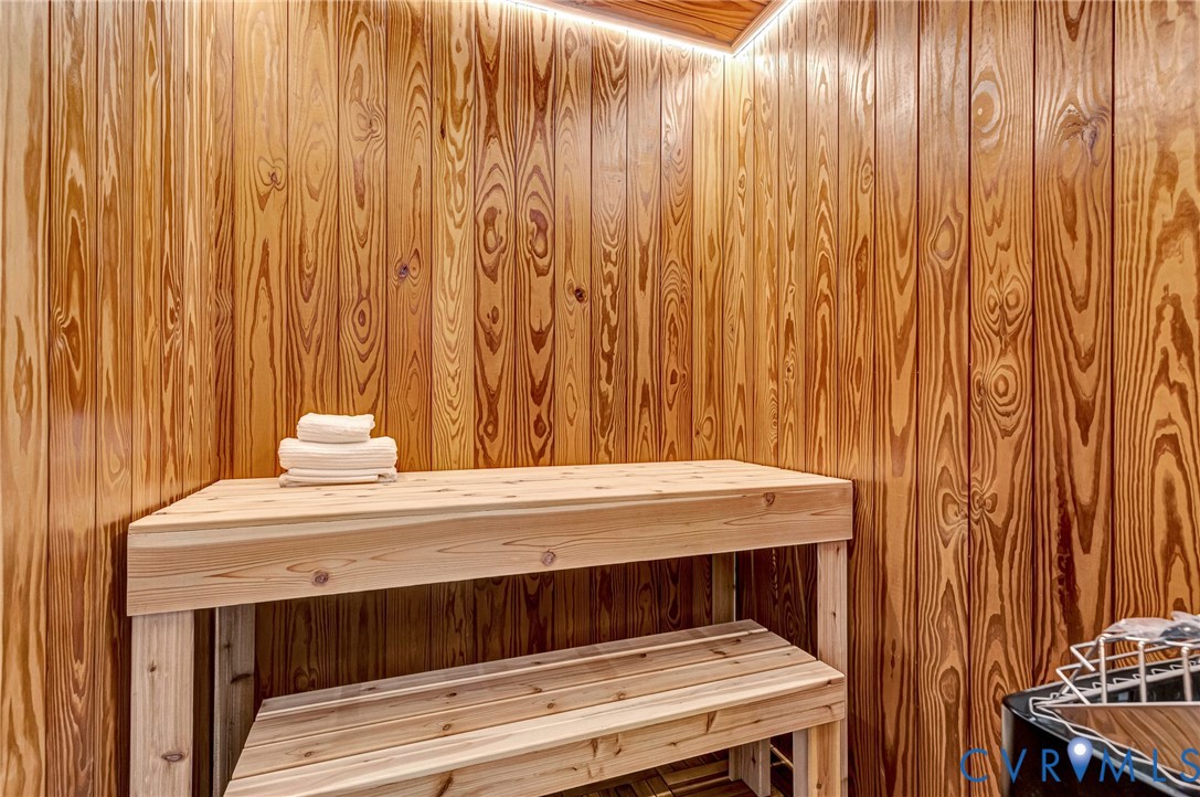 Sauna featuring vertical wood paneling, tiered wood bench seating, and integrated cove lighting