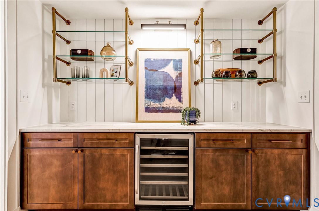 Custom cabinetry with integrated wine cooler, stone countertop, vertical shiplap wall paneling, and metallic wall-mounted shelving units