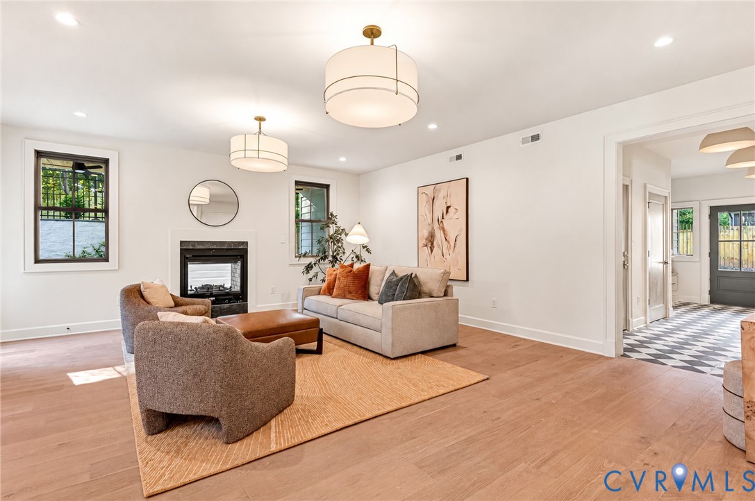 Living area featuring wood-finish flooring, two large drum-style pendant light fixtures, a fireplace with a dark stone surround, and recessed lighting