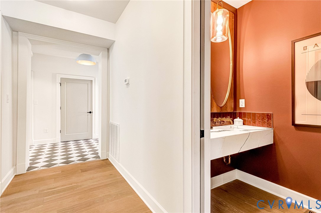 Floating vanity with a stone countertop, oval wall-mounted mirror, pendant lighting, and wood-finish flooring