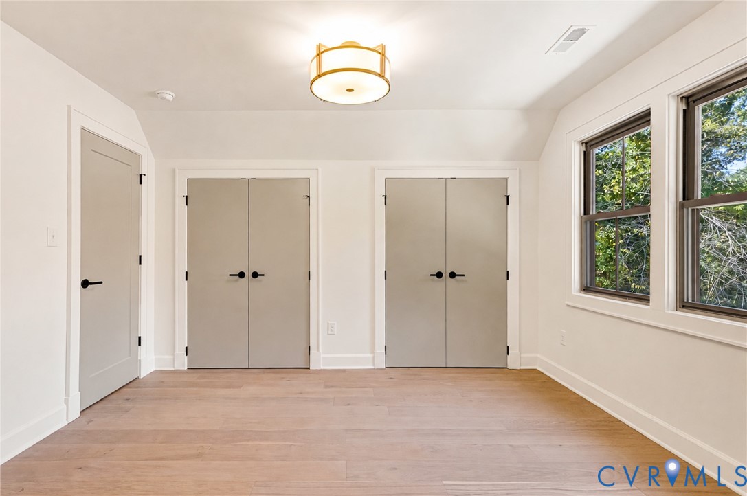 Wood-finish flooring, two sets of double-door closets, contemporary drum ceiling light fixture, neutral interior paint, and double-hung windows