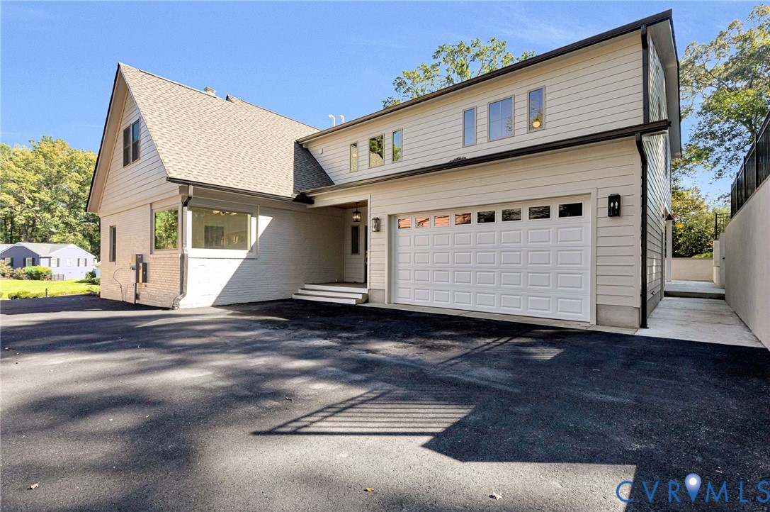 Exterior featuring a multi-gabled roofline, horizontal siding, brick facade, asphalt-paved driveway, and an attached two-car garage