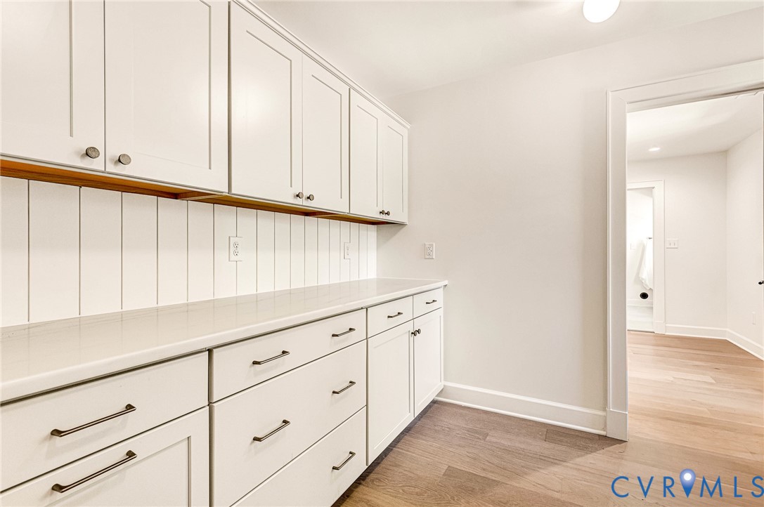 Custom cabinetry with matte finish hardware, quartz countertop, vertical wood-panel backsplash, and wood-finish flooring