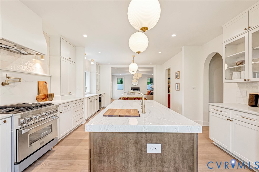 Kitchen featuring a central island with a stone countertop, custom white cabinetry, a professional-grade stainless steel range with a pot filler, wood-finish flooring, and globe pendant lighting