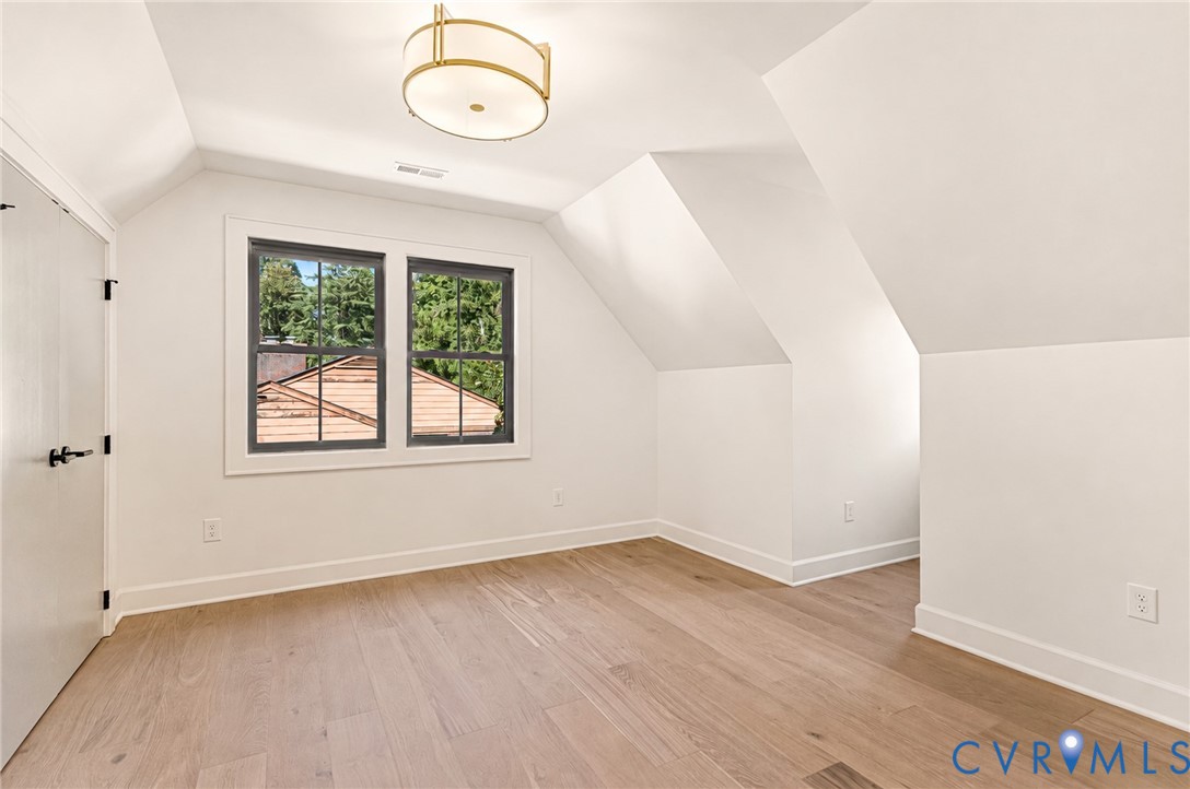 Room featuring wood-finish flooring, vaulted ceilings, multi-pane windows with dark frames, and a drum-style ceiling light fixture