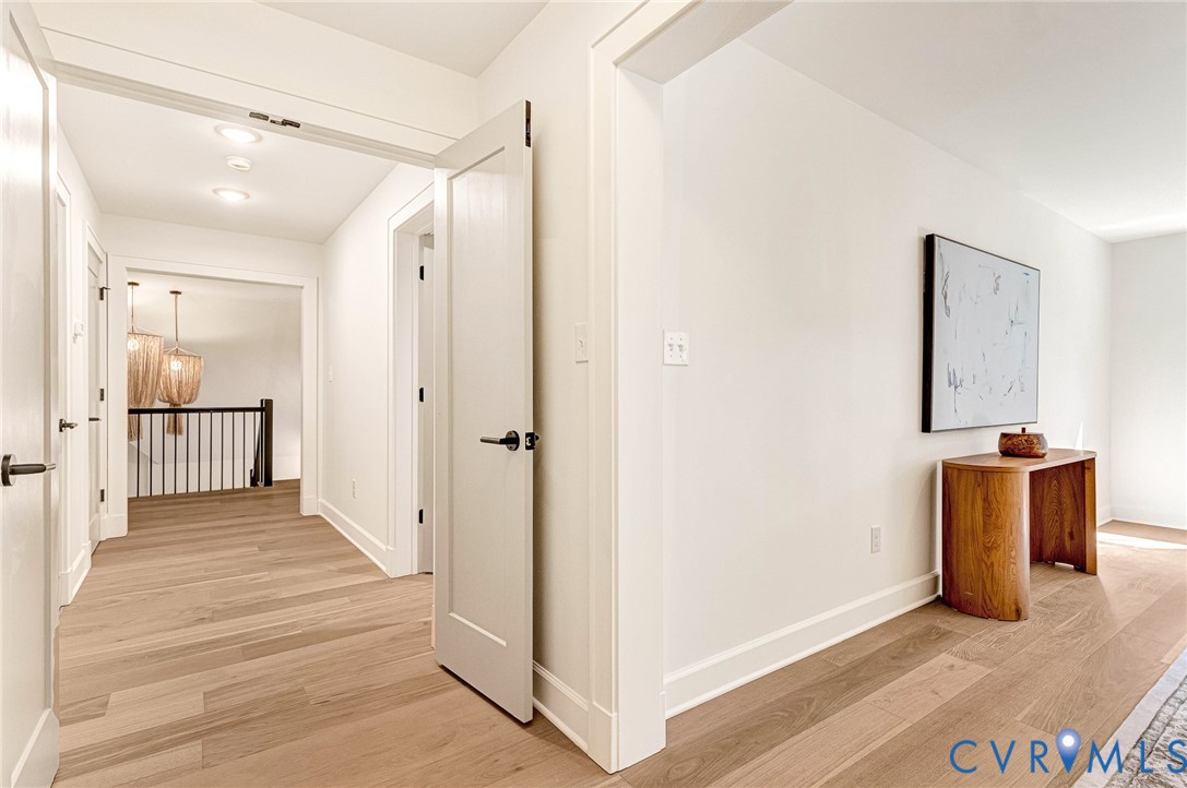 Hallway featuring light wood-finish flooring, shaker-style interior doors with matte black hardware, and crisp white trim
