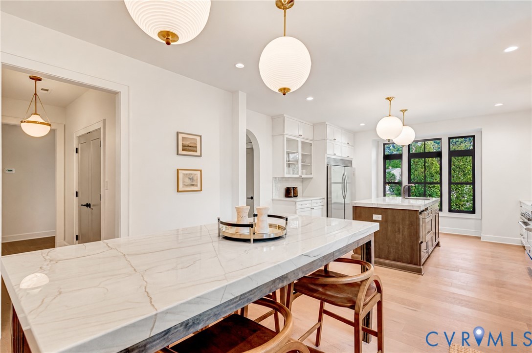 Kitchen featuring an island with a white stone-surface countertop, wood-finish cabinetry, recessed lighting, spherical pendant fixtures, and large windows with black frames