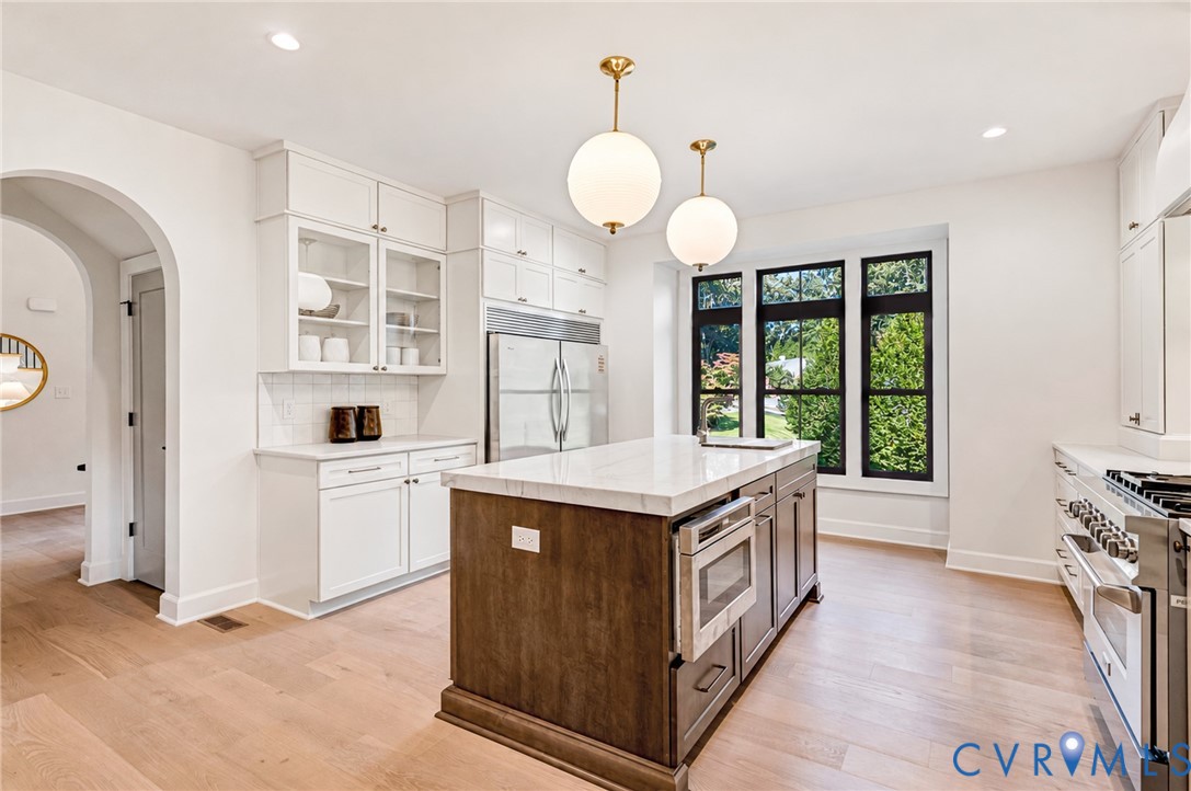 Kitchen featuring a center island with stone-style countertops, wood-finish flooring, custom shaker-style cabinetry, professional-grade stainless steel range, and dual globe pendant lighting