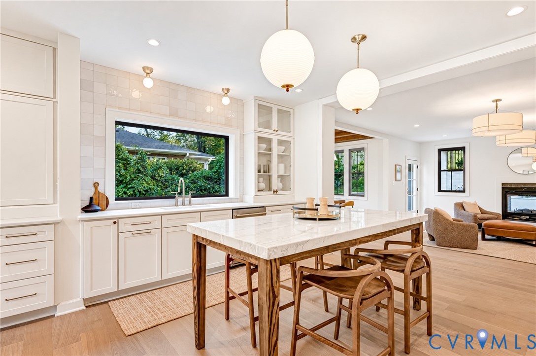 Kitchen featuring crisp white cabinetry, stone-topped island with wood-finished legs, square-tile backsplash, globe pendant lighting, and wood-finish flooring Kitchen featuring crisp white cabinetry, stone-topped island with wood-finished legs, square-tile backsplash, globe pendant lighting, and wood-finish flooring