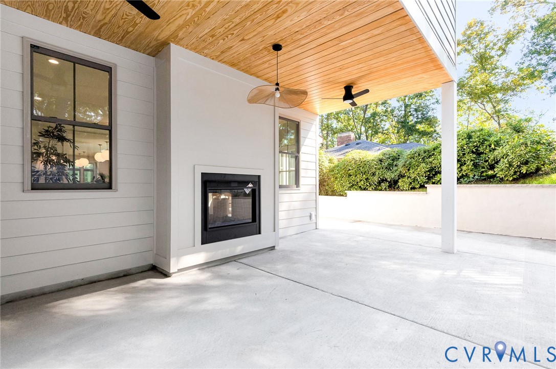 Covered patio featuring a wood-plank ceiling, built-in outdoor fireplace, concrete flooring, ceiling fan, and pendant lighting