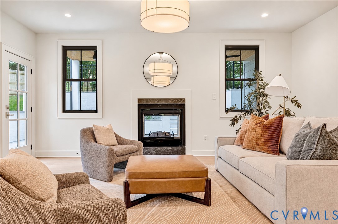 Fireplace with stone-style surround, double-hung windows with black frames, recessed ceiling lighting, drum-style pendant light, and glass-paned exterior door