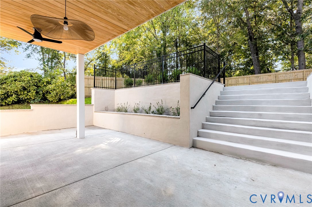 Covered concrete patio featuring a wood-finished ceiling, overhead lighting, integrated retaining walls, and a staircase with a metal handrail