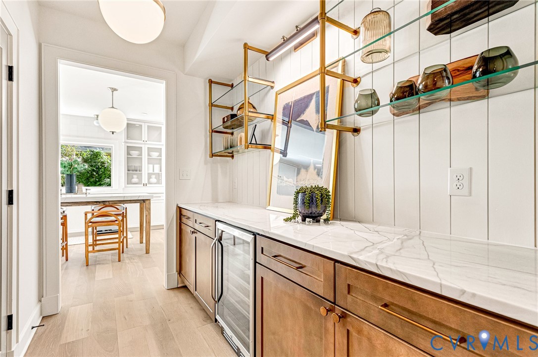 Custom cabinetry featuring integrated wine refrigerator, stone-patterned countertops, vertical shiplap wall paneling, and metallic open-frame shelving with glass surfaces
