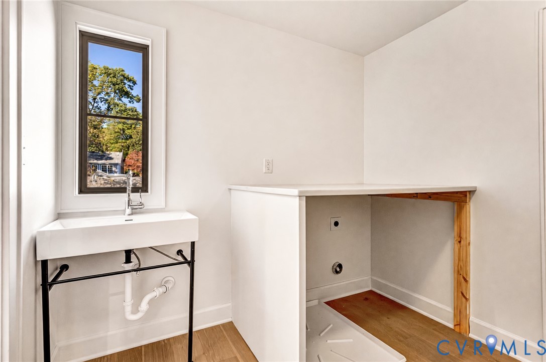 Utility area featuring a wall-mounted rectangular sink with a chrome faucet, a matte black metal console stand, and wood-finish flooring