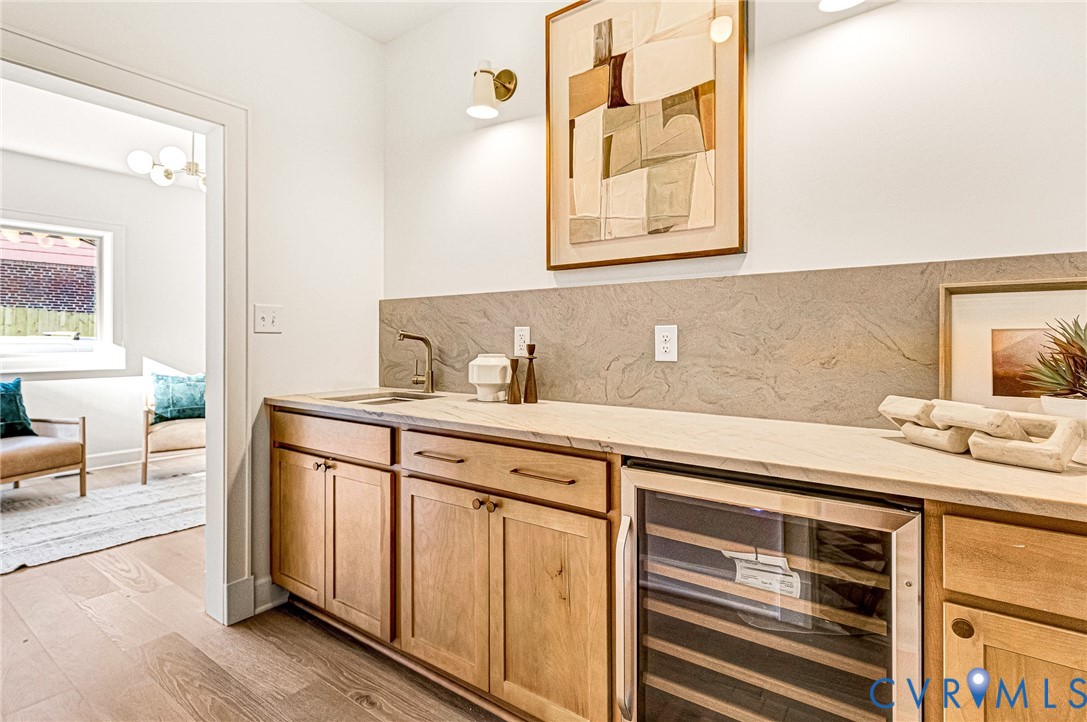 Custom cabinetry with wood finish, stone-surface countertop, integrated beverage refrigerator, stone backsplash, and wall-mounted metal light fixtures