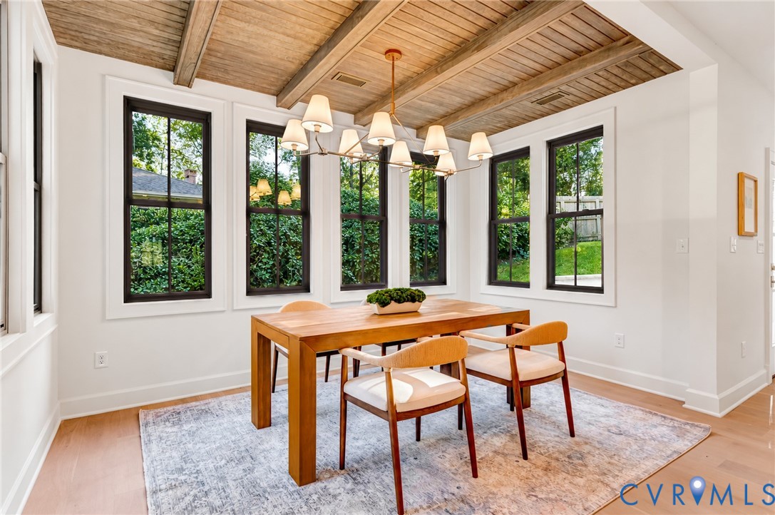 Vaulted ceiling with exposed wood beams, multi-light linear chandelier, and expansive windows with black frames