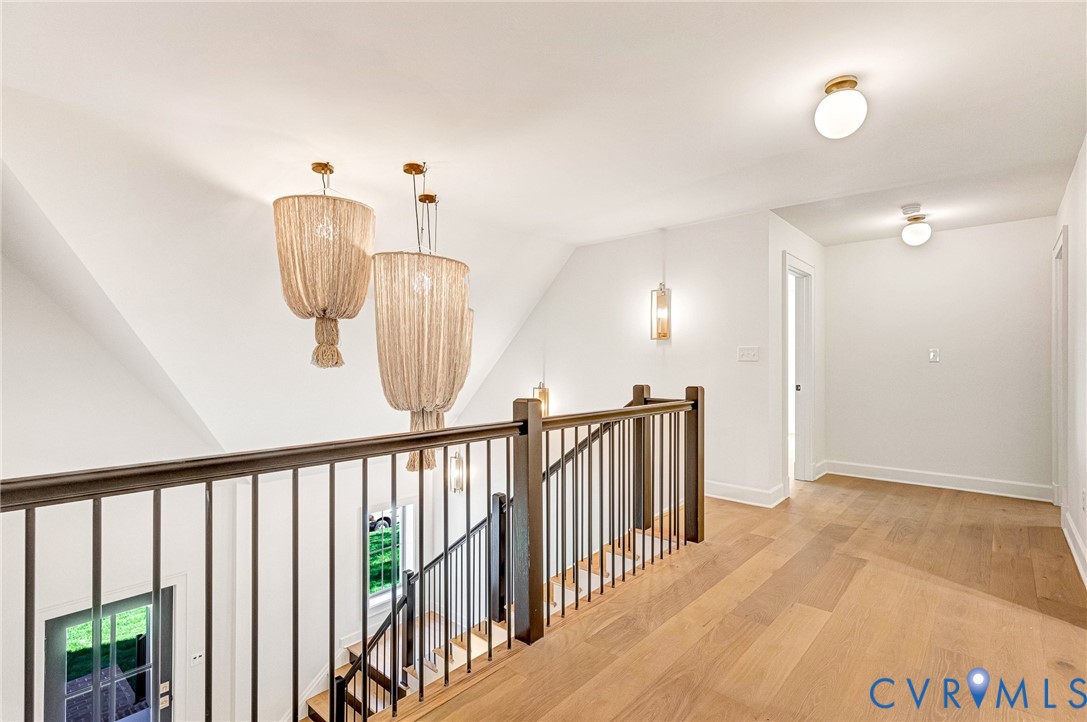 Landing area featuring wood-finish flooring, metal railing, woven pendant lighting, flush-mount globe fixtures, and wall-mounted sconces