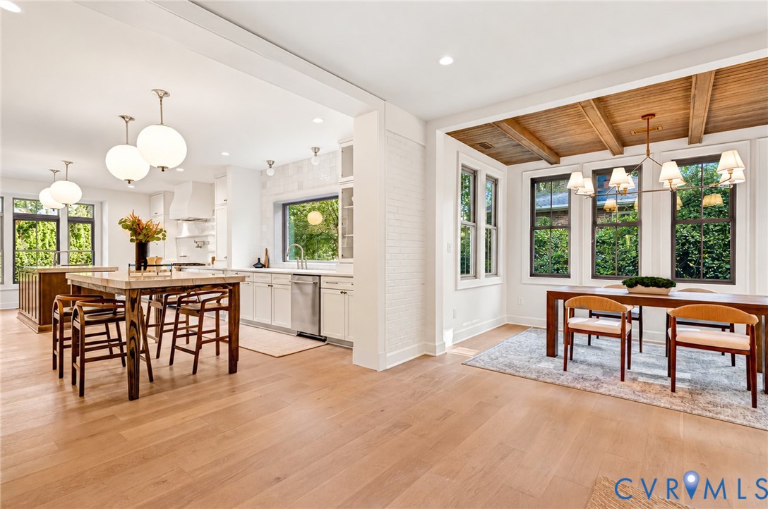 Open-concept kitchen and dining area featuring wood-finish flooring, wood-beamed ceiling, white painted brick architectural accents, and polished surface countertops