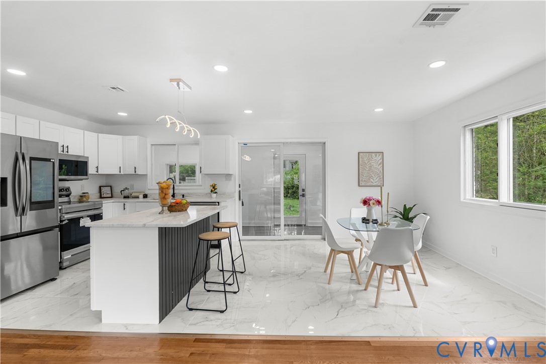 Modern kitchen featuring stainless steel appliances, white cabinetry, a kitchen island with seating, and white marble-look flooring