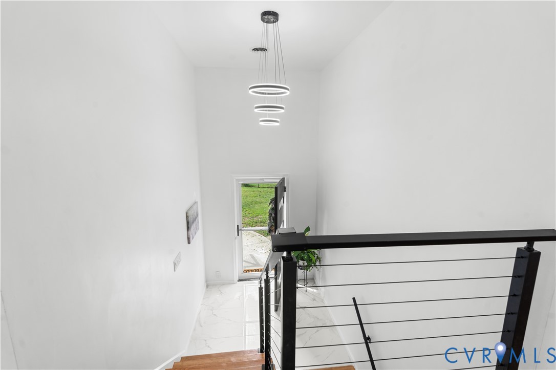 Hardwood staircase with cable railing, modern ceiling-mounted light fixture, white wall finishes, and tile flooring at landing